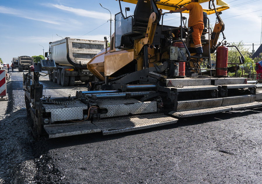 worker operating asphalt paver machine during road construction and repairing works. a paver finisher, asphalt finisher or paving machine placing a layer of asphalt.