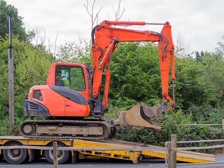 small tracked excavator being loaded onto a flatbed transporter.